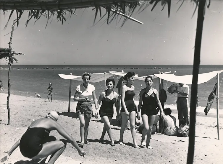 Fotografía en blanco y negro de cuatro chicas jóvenes en bañador paseando por una playa.