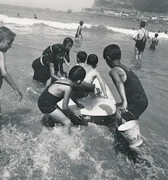 Fotografía en blanco y negro de unos niños jugando en el agua del mar a principios de los años 30.