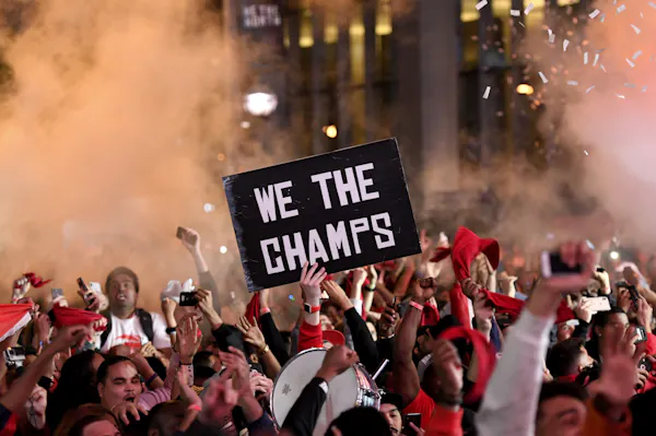 A crowd of people celebrate while holding a sign that says 'We the champs'