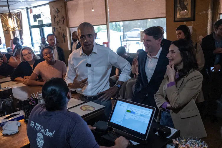 Three people stand at a counter in a taco restaurant