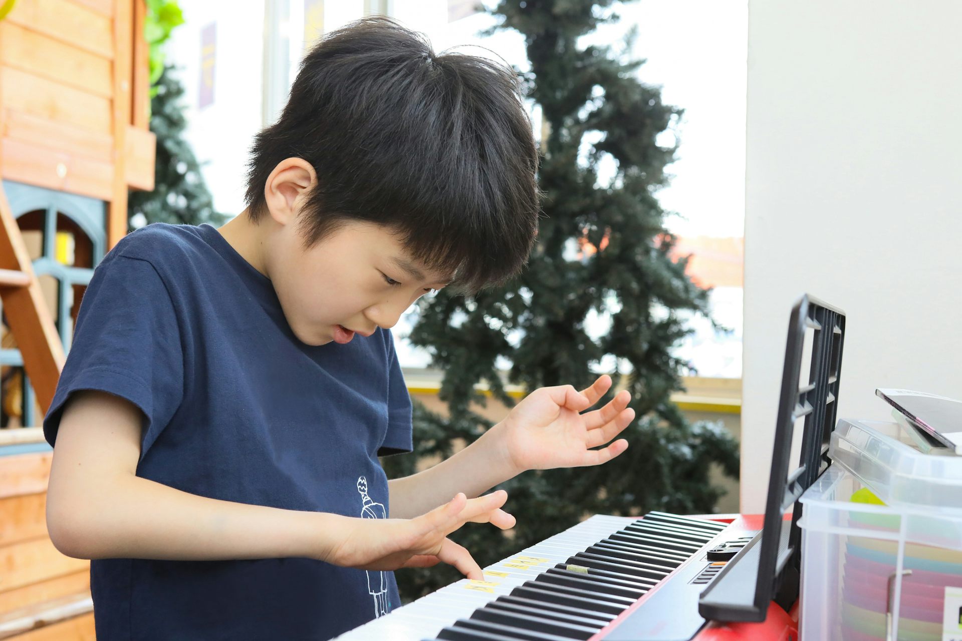 A young boy wearing a blue shirt presses on a key of a piano.