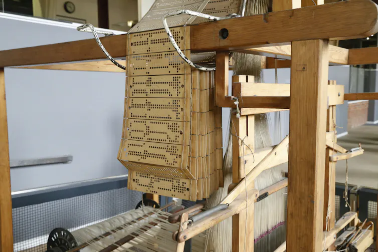 A series of punches of beige cards hang over a wooden apparatus