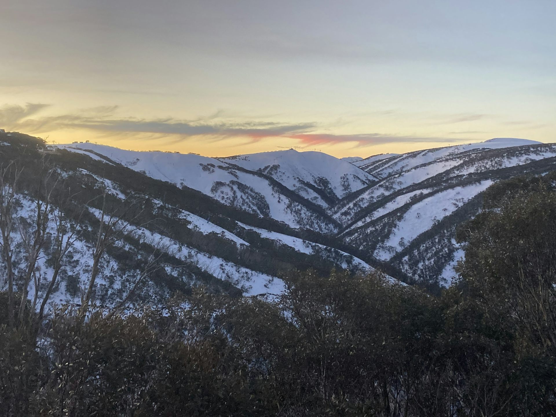 A view of snow-covered mountains with a sunset in the background.