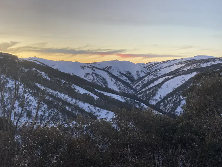 A view of snow-covered mountains with a sunset in the background.