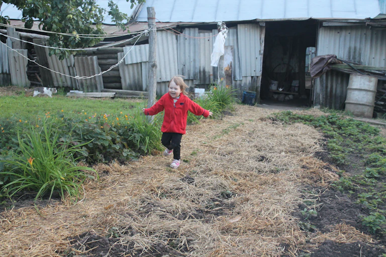 A child in a warm jacket runs along a garden bed.