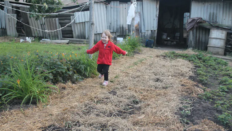 A child in a warm jacket runs along a garden bed.