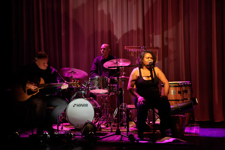 A woman sings onstage while a band plays alongside her.