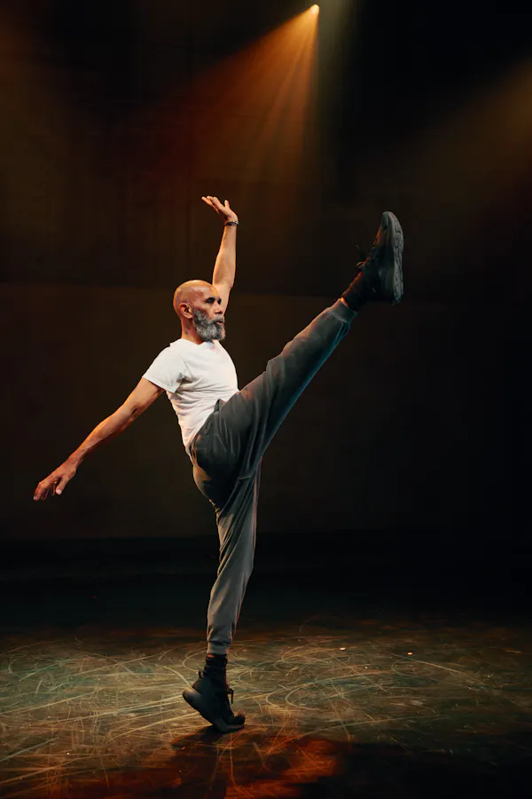 A man dances onstage, lifting his right leg high in the air.