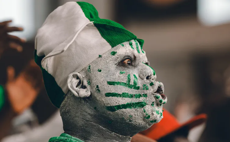 An African man in profile makes an exaggerated shocked expression, his face painted green and white.