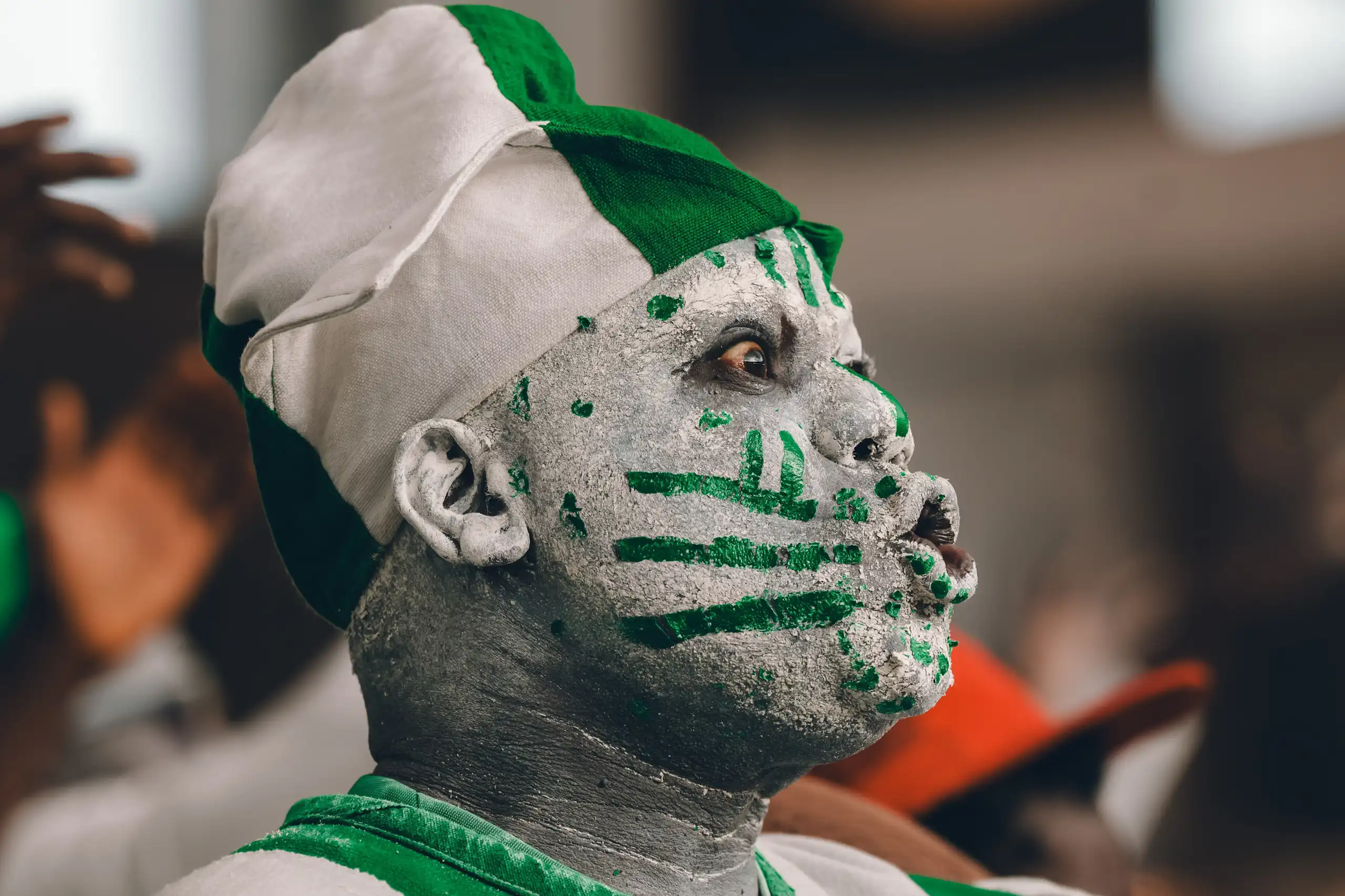 An African man in profile makes an exaggerated shocked expression, his face painted green and white.