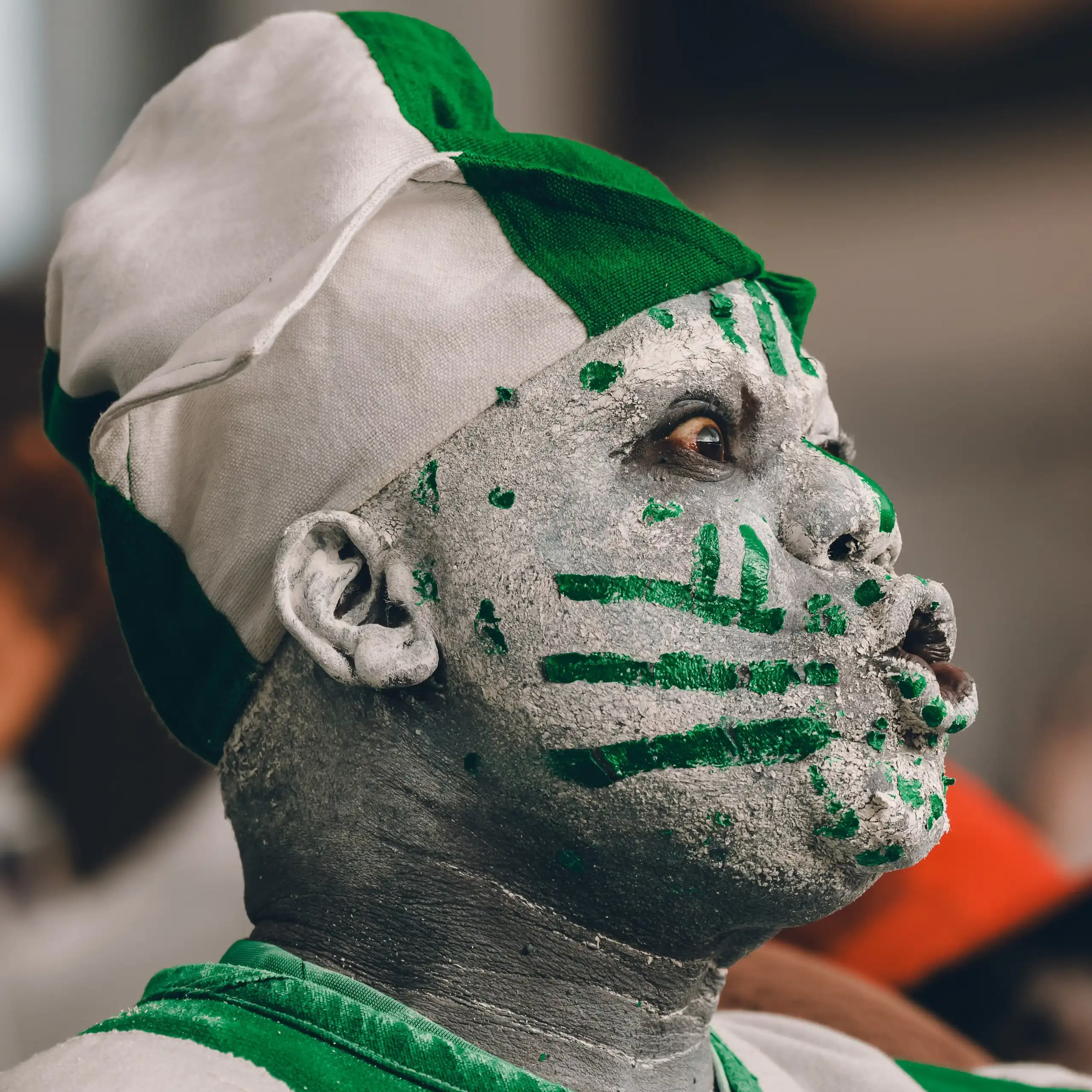 An African man in profile makes an exaggerated shocked expression, his face painted green and white.