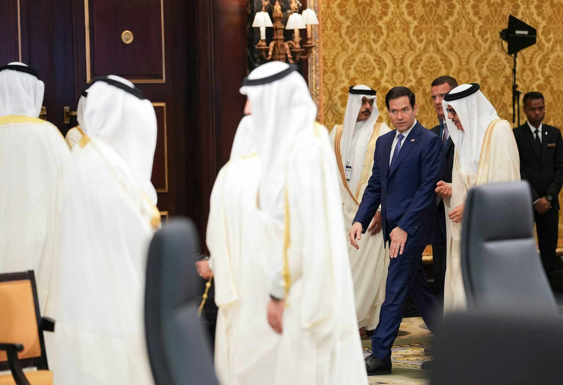 A group of men in traditional Arab robes meet with a man in a western-style business suit.