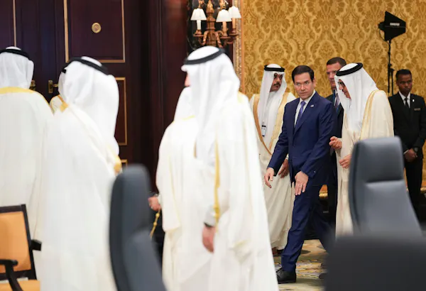 A group of men in traditional Arab robes meet with a man in a western-style business suit.
