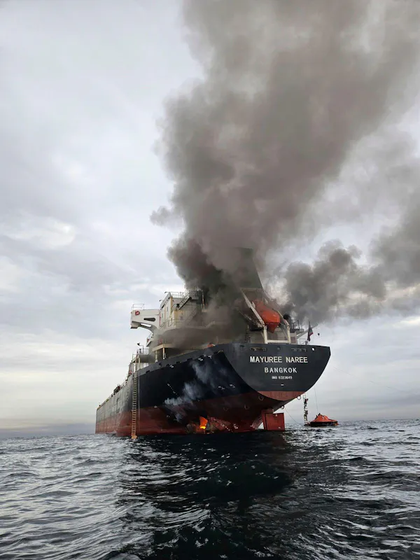 A ship with smoke billowing out after being hit by a missile.