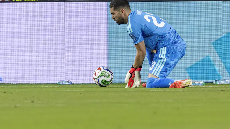 A goalkeeper in blue parries a ball.