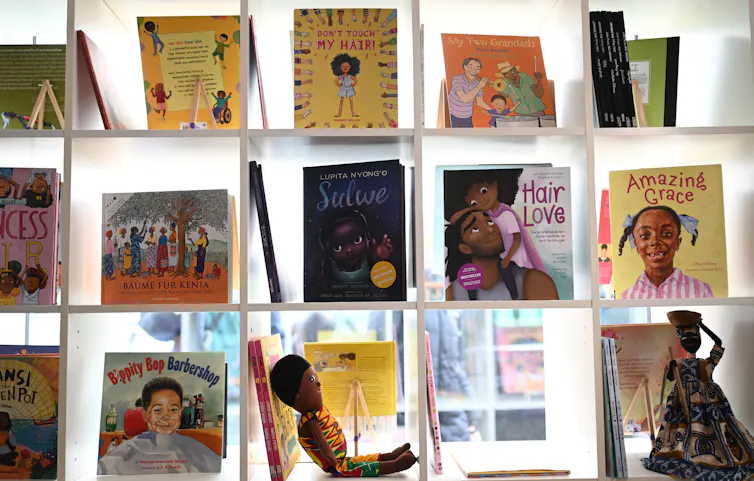 Three rows of children's books that have covers of Black children are seen on display, with sunlight behind them.