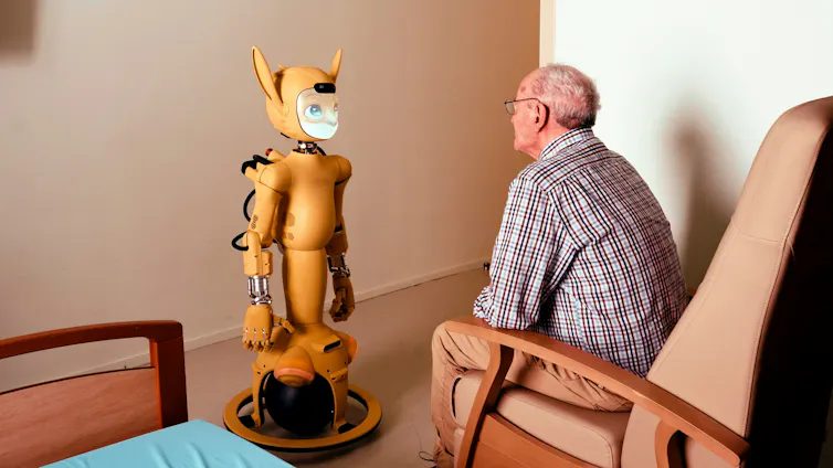 A yellow robot with a human-fox face stares at an older man who sits in a chair.