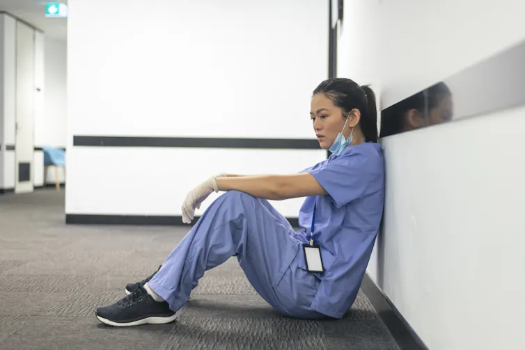 A female nurse of asian descent sits on the hospital hallway floor.