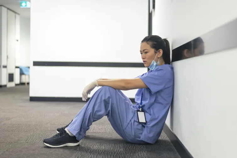 A female nurse of asian descent sits on the hospital hallway floor.