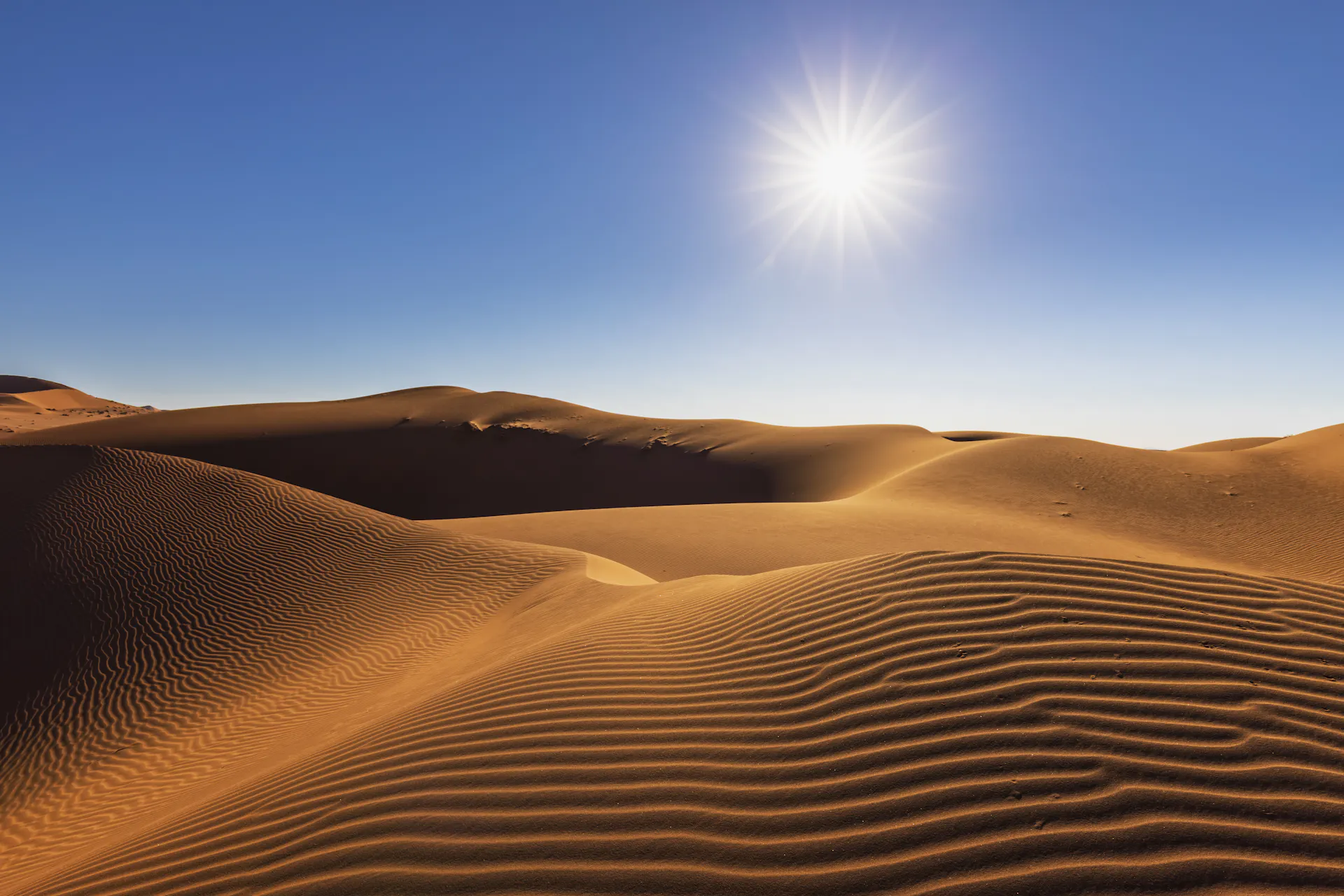 Hills made of sand sit beneath a cloudless, sunny sky