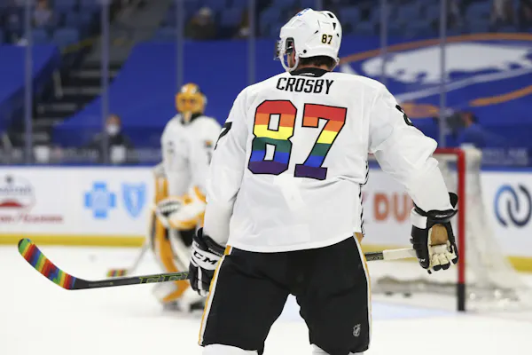 A hockey player wears a jersey with a rainbow-coloured number on the back, holding a hockey stick with rainbow tape on it