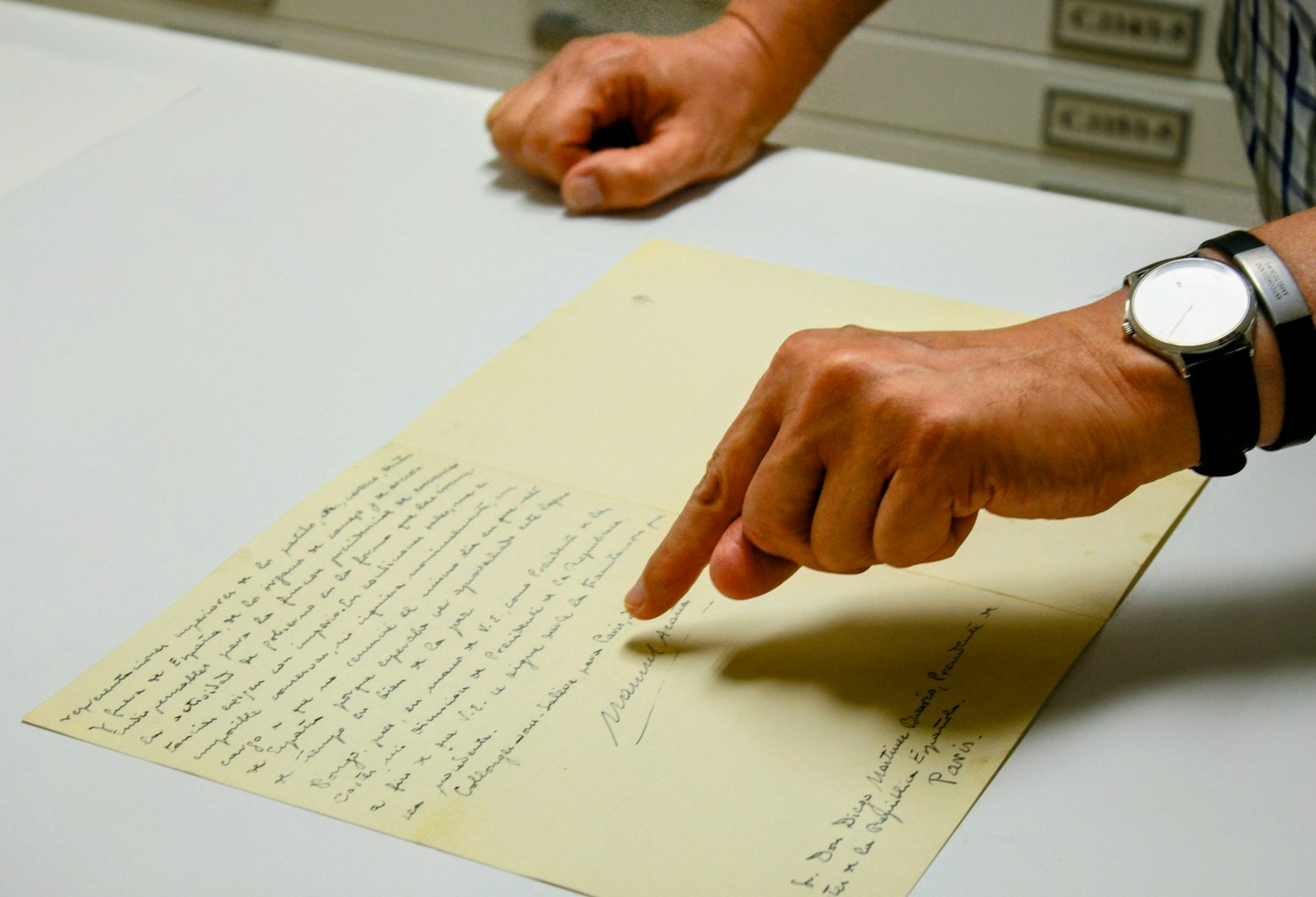 Una mano señala una firma en una carta colocada sobre una mesa.