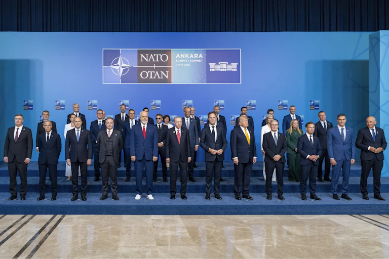 Multiple heads of state pose for a photo in front of a background that features the Nato logo