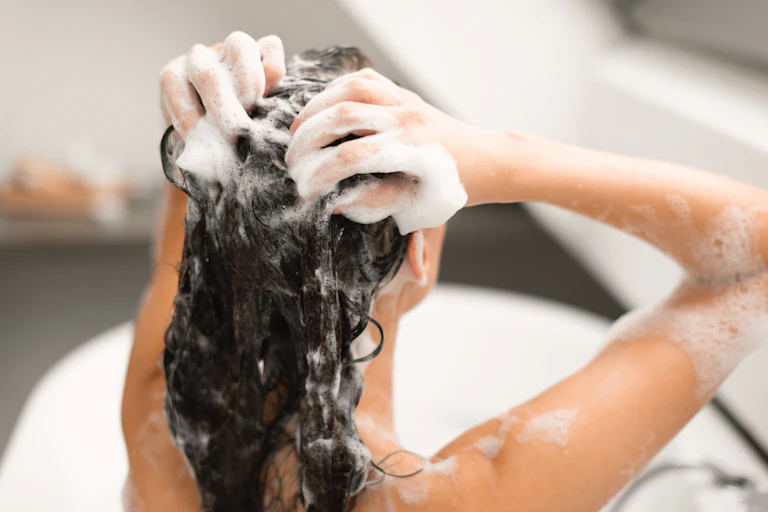 Photo d’une jeune femme qui se lave les cheveux, assise dos dans une baignoire.