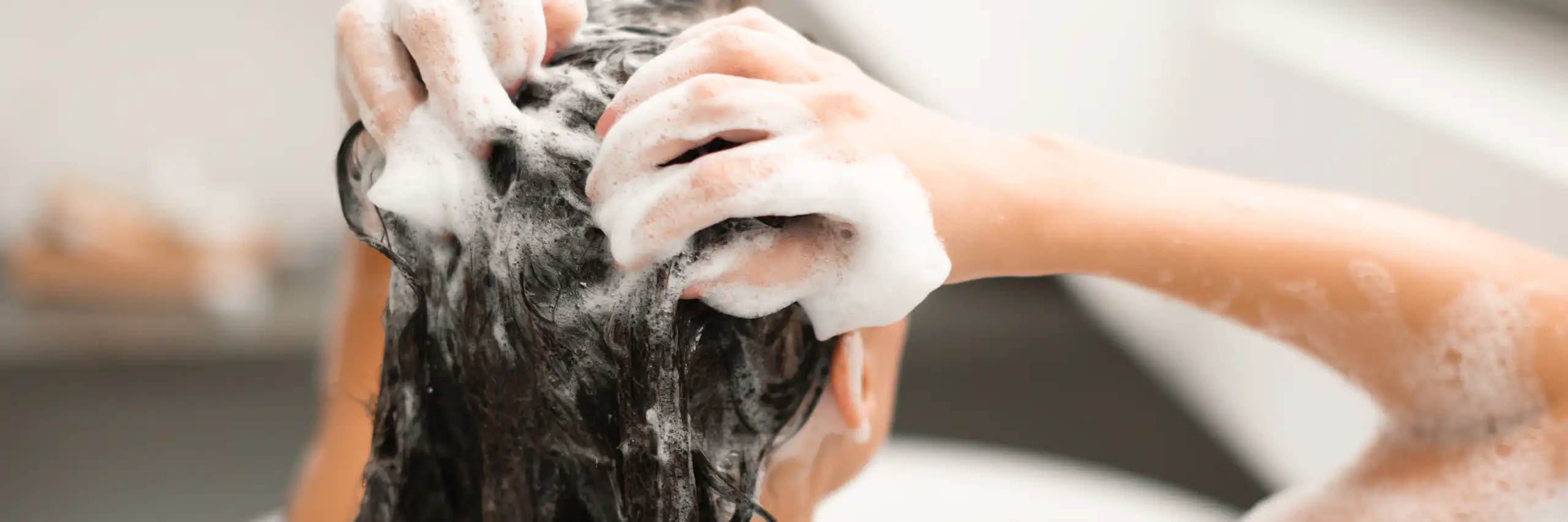 Photo d’une jeune femme qui se lave les cheveux, assise dos dans une baignoire.