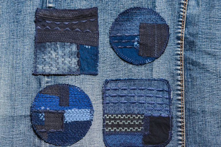 denim jeans, close up, four blue stitched patches to mend rips