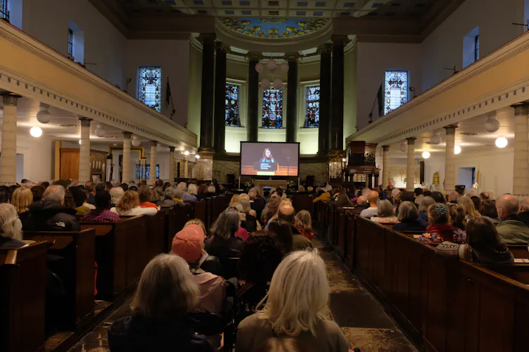 grand inside of building, people sat looking at screen at far end of room
