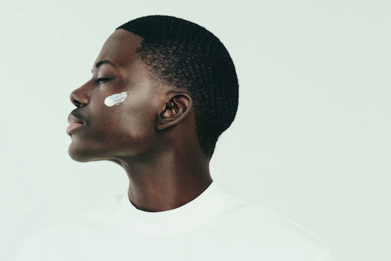 Profile shot of a man with moisturiser on his cheekbone. White background.