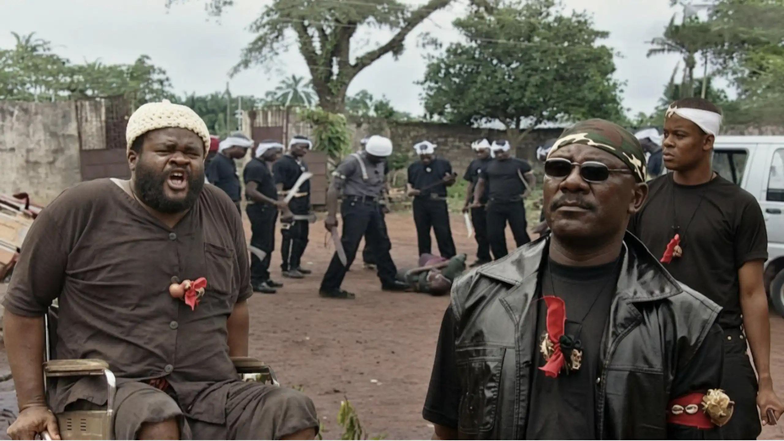 Two men in the foreground, behind them a group of men wearing white headbands, around a man who is lying on the ground