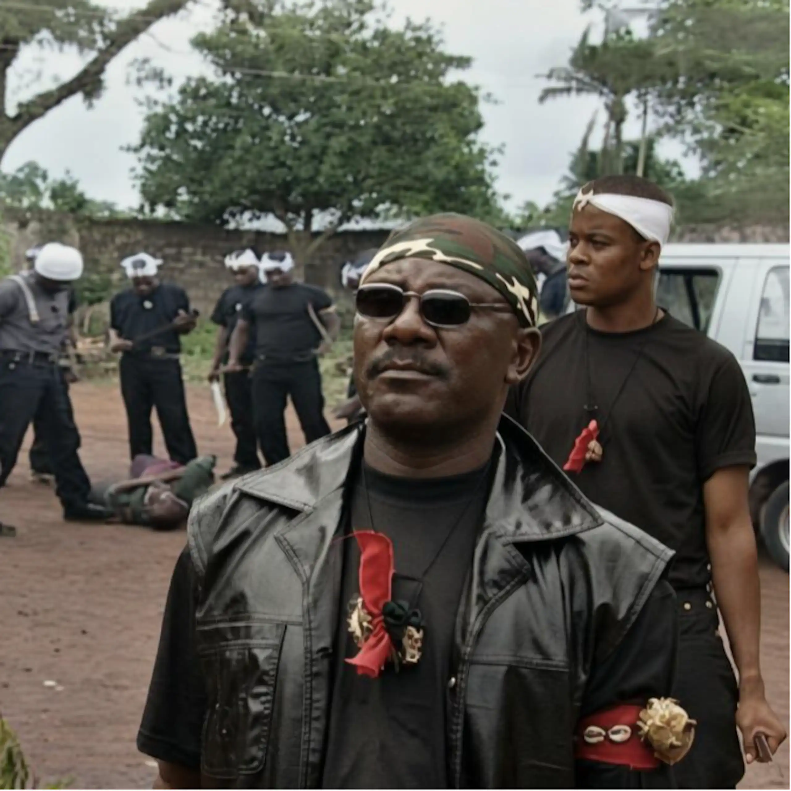 Two men in the foreground, behind them a group of men wearing white headbands, around a man who is lying on the ground