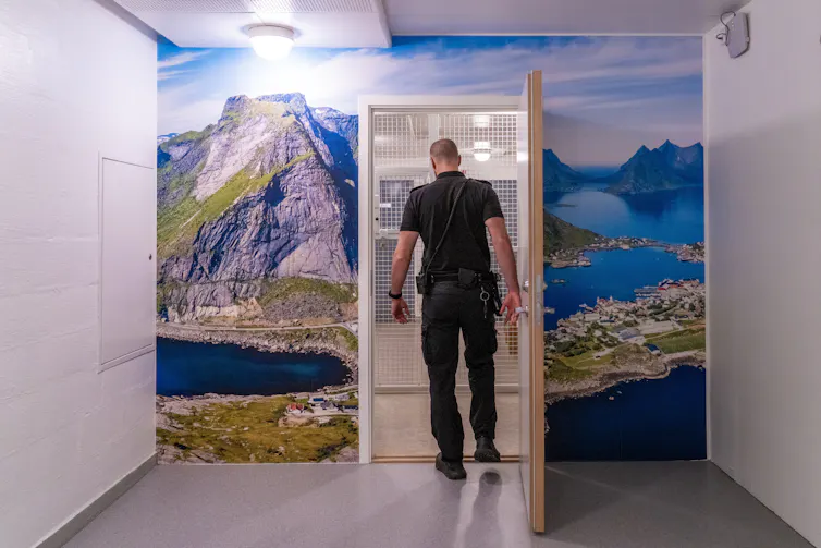 A prison guard opening a door on a wall covered in a photograph of a beautiful landscape