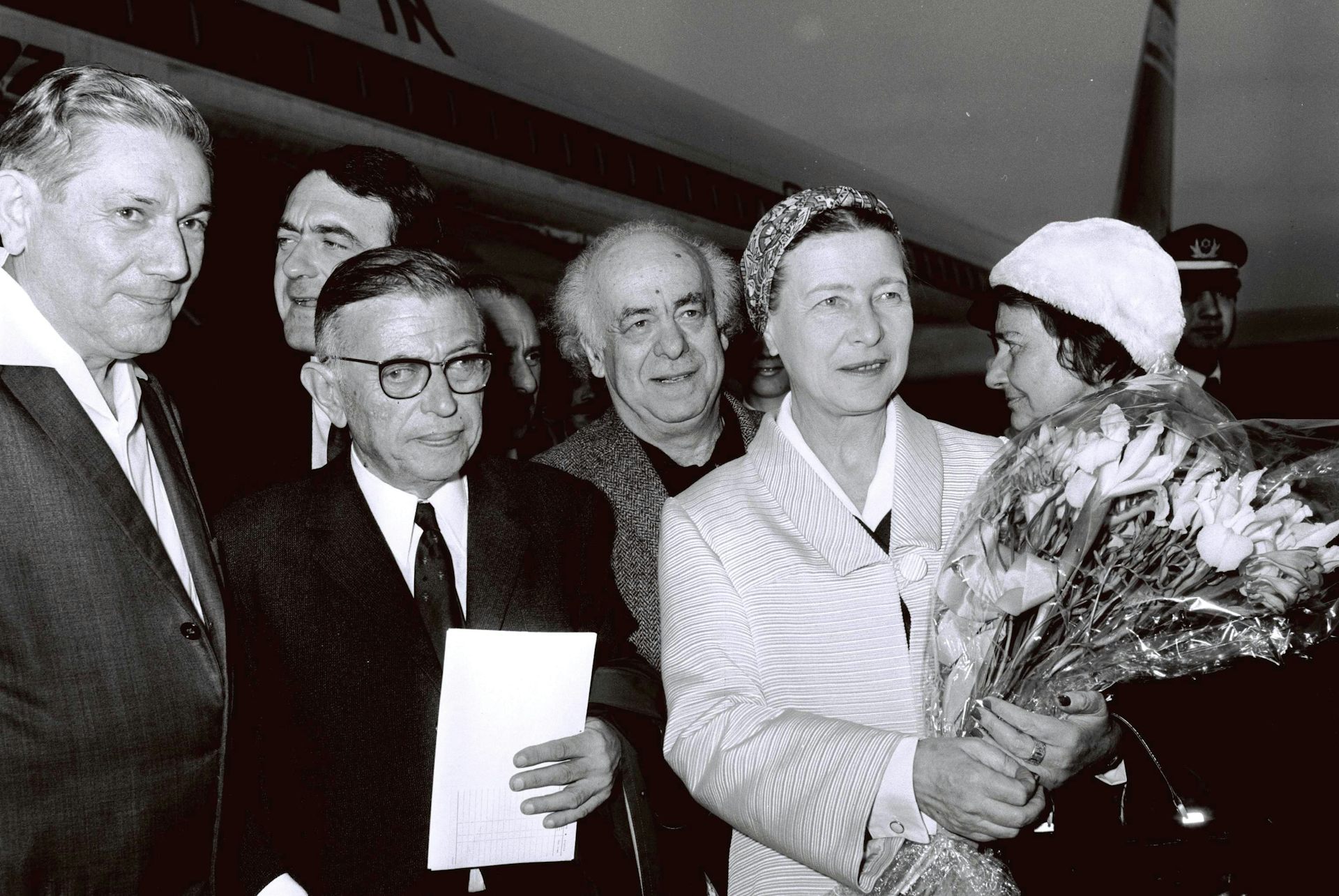 Una mujer sostiene un ramo de flores junto a otros hombres y mujeres en una foto en blanco y negro.