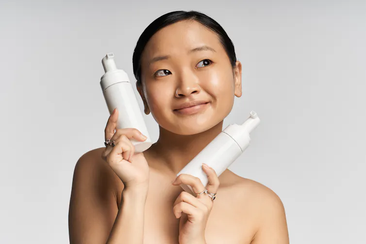 Woman holds two skincare bottles up to her face