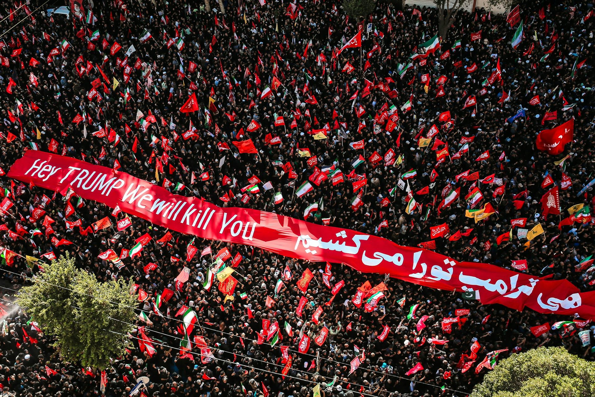 Aerial shot of a crowd in the city of Mashhad displaying a banner reading: 'Hey Trump, we will kill you'.