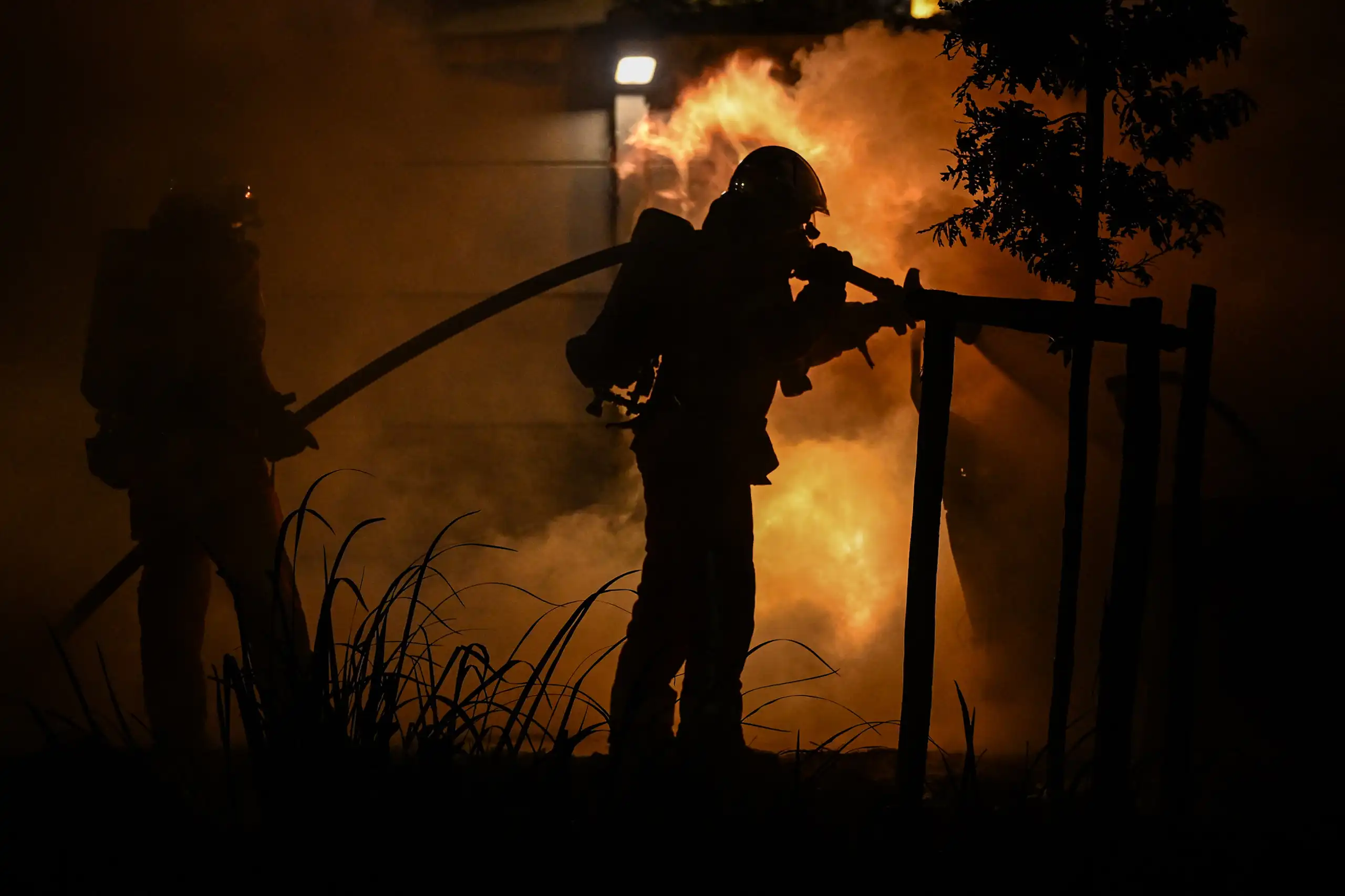 pompier et sa lance à incendie devant les flammes