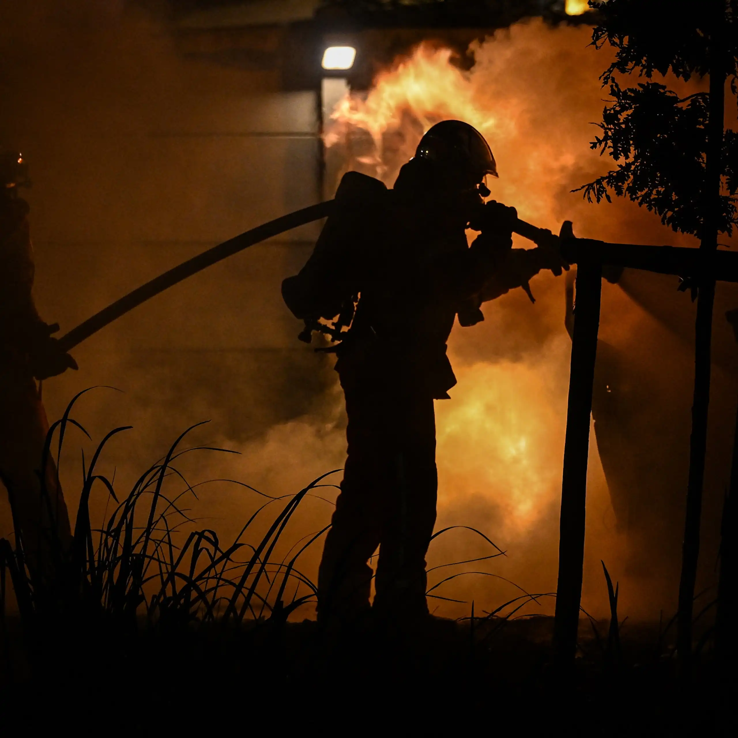 pompier et sa lance à incendie devant les flammes