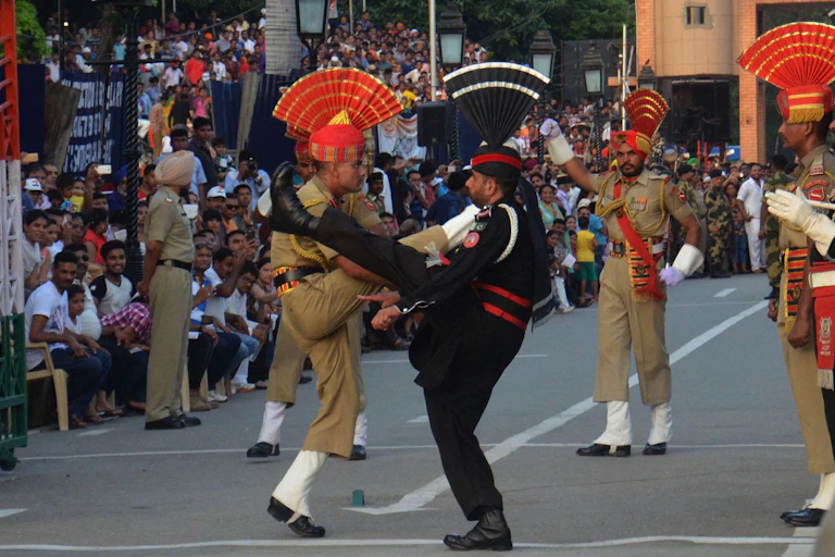 Pakistani and Indian soldiers wearing ceremonial uniforms kick their legs high.