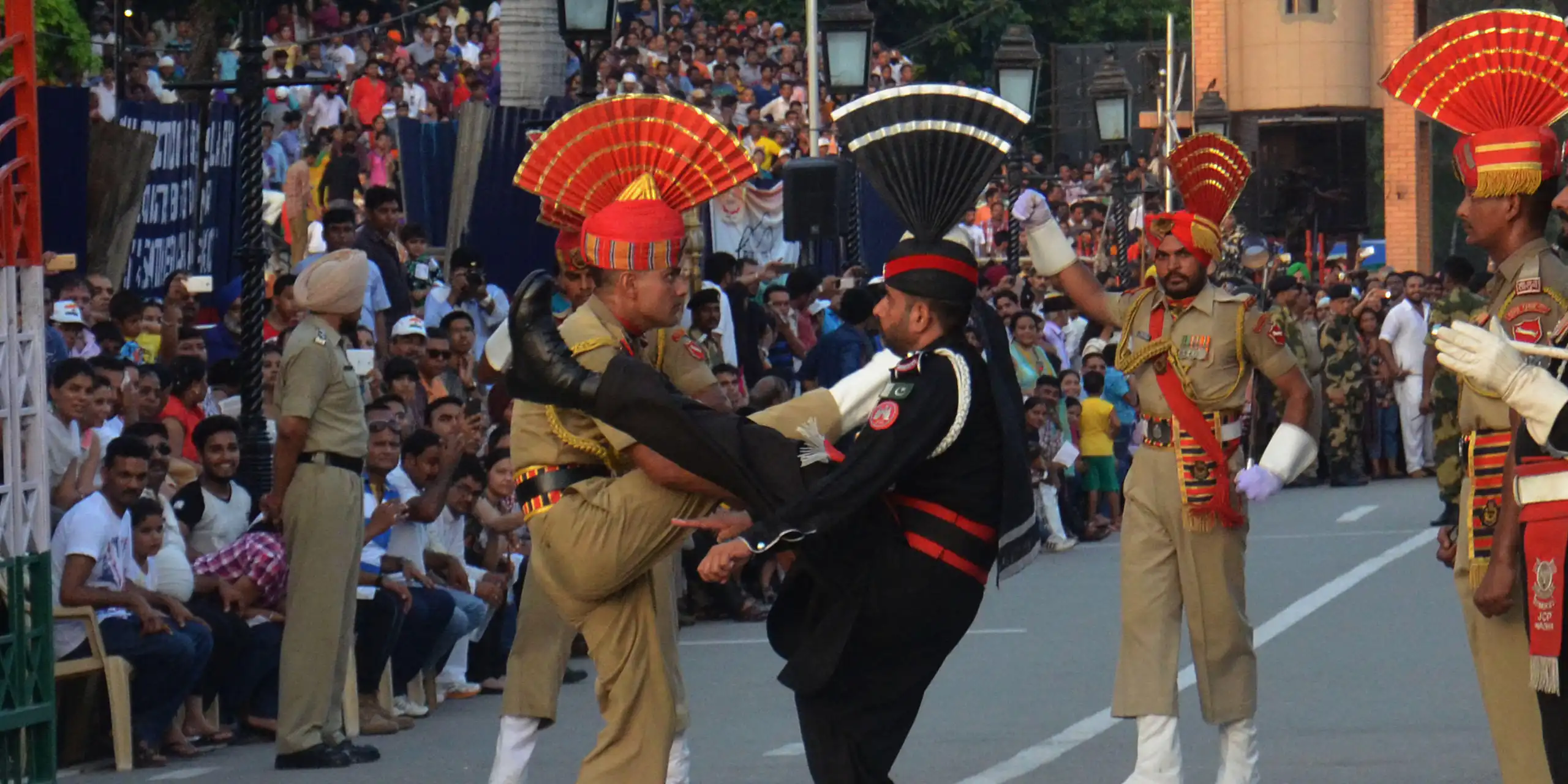 Pakistani and Indian soldiers wearing ceremonial uniforms kick their legs high.