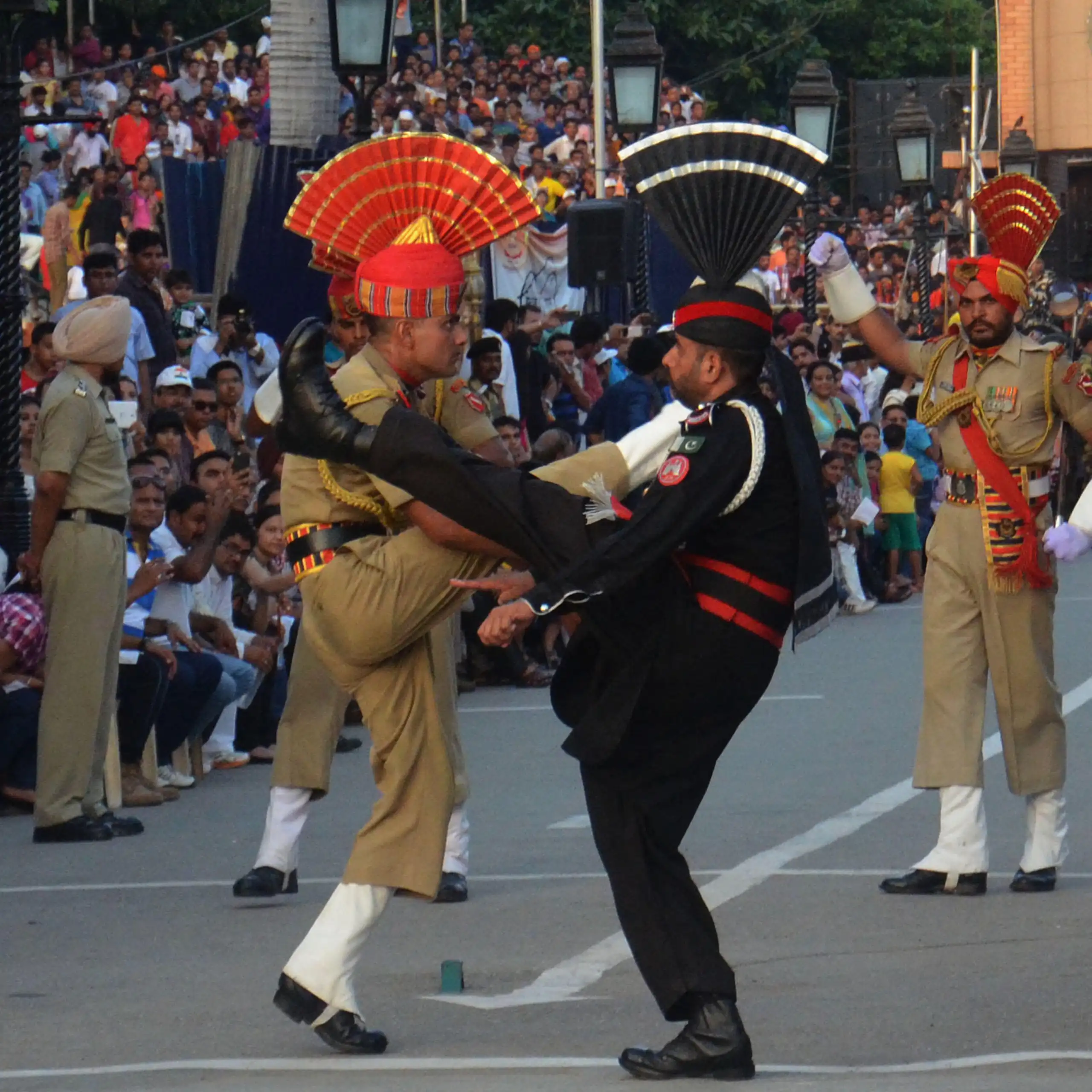 Pakistani and Indian soldiers wearing ceremonial uniforms kick their legs high.