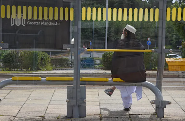 man sitting alone at a bus stop decorated with yellow bee network livery.