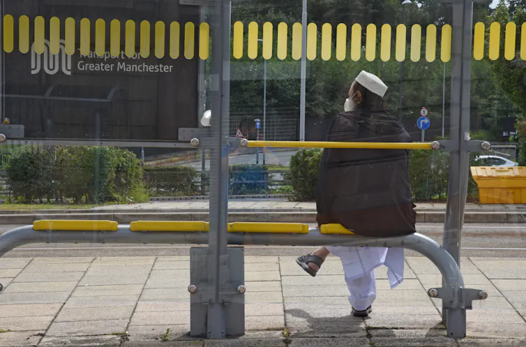 man sitting alone at a bus stop decorated with yellow bee network livery.