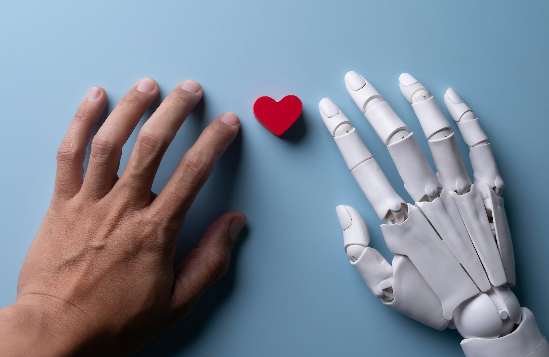 Una mà humana i una robòtica amb un xicotet cor enmig.