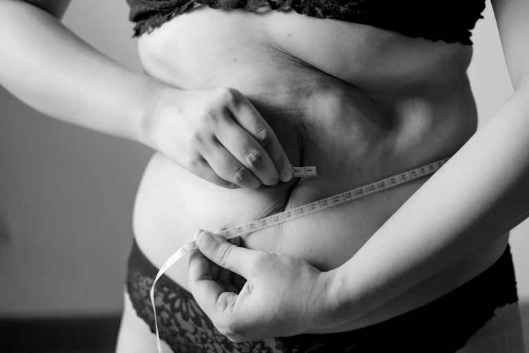 A close-up of the midriff of a woman as she measures her waist with a measuring tape.