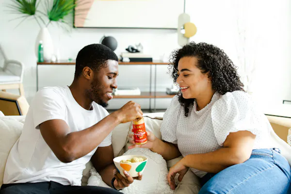 A couple on a date sitting on a couch and sharing some snacks.