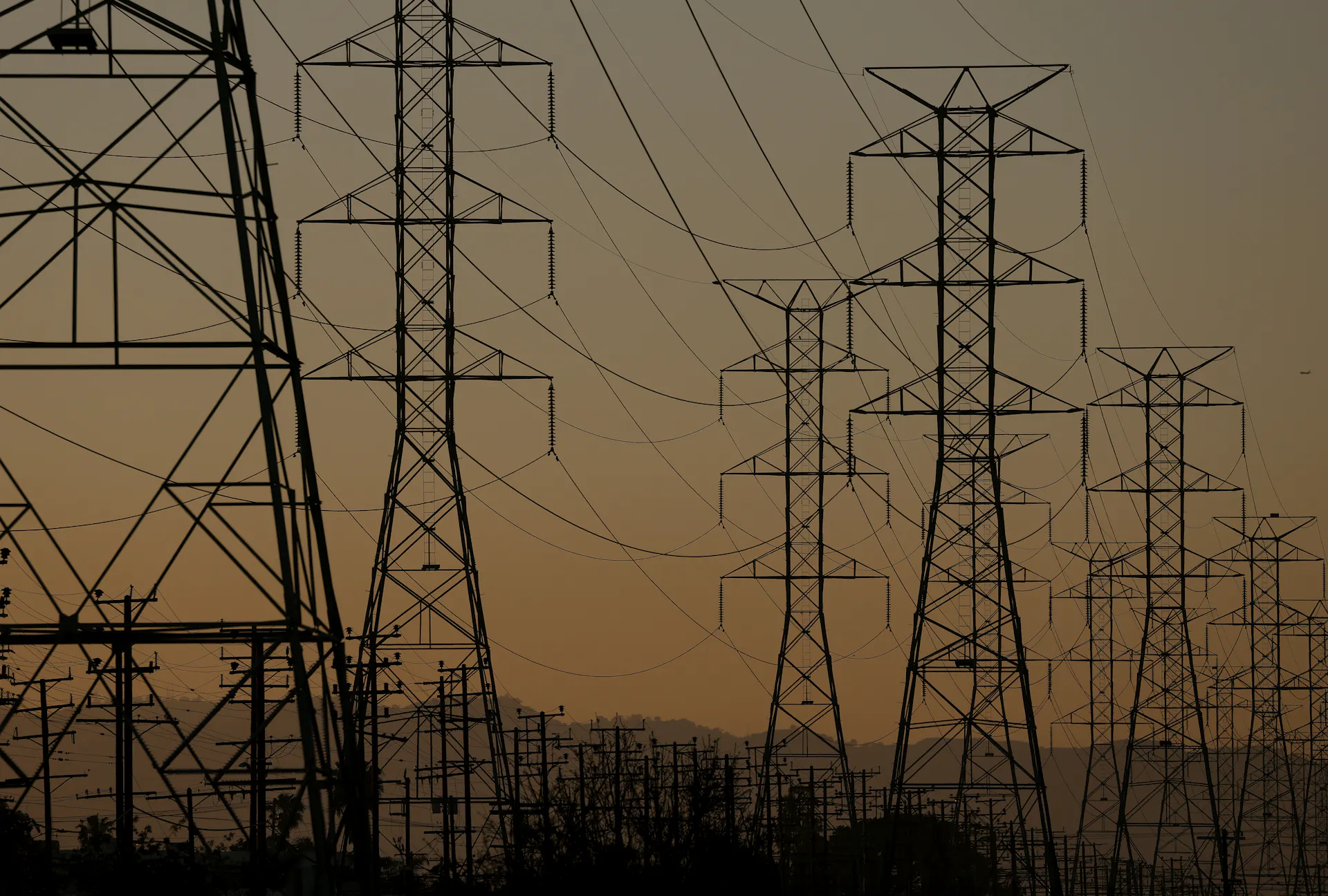 Rows of transmission towers and power lines silhouetted against a hazy sky
