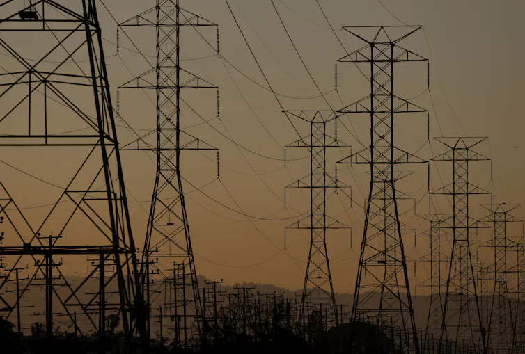 Rows of transmission towers and power lines silhouetted against a hazy sky